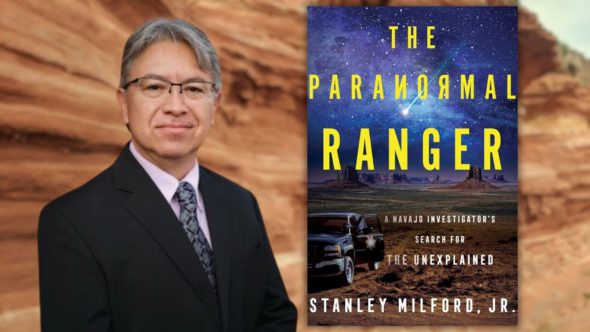 The author, Stanley Milford, Jr., in a suit with an image of his book cover next to him, The Paranormal Ranger by Stanley Milford, Jr. The cover features a desert landscape at night with a starry sky, a vehicle.