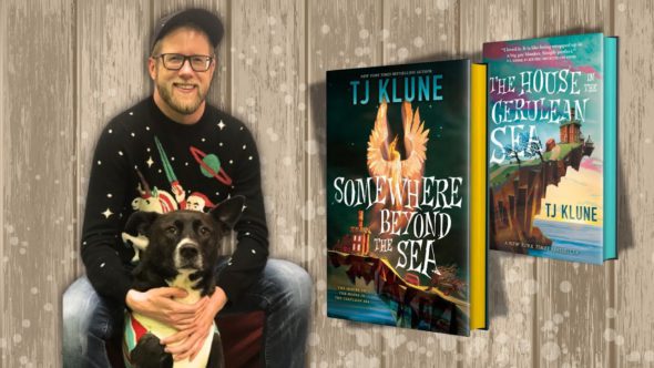 The author, TJ Klune, wearing a baseball hat, glasses, and a black sweater with their black and white dog. Also, features book cover images of The House in the Cerulean Sea and Somewhere Beyond the Sea.