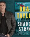 Author Brad Taylor with short dark hair and some grey on the sides. He's wearing a brown leather jacket open with a black button up shirt and jeans. Features the book cover of Shadow Strike by Brad Taylor.