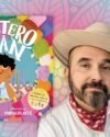 Author, Lucky Diaz, with a tan cowboy hat, red bandana around the collar of a his white button up shirt. Book cover of Paletero Man. Background is bright blues and pinks with flower shapes.